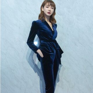 Femme portant une veste kimono bleue et un pantalon en velours avec une main dans la poche du pantalon.