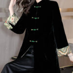 Veste Kimono en velours noir avec attaches vertes et manches motif fleuri japonisant porté par une femme assise avec un pantalon en simili cuir noir