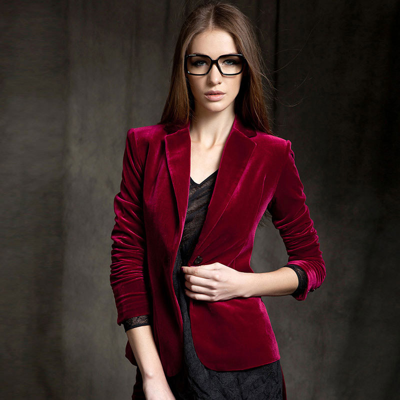 femme d'origine caucasienne portant un blazer en velours rouge sombre et des lunettes, sur fond marron