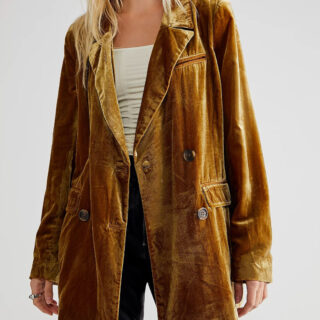 blazer en velours jaune moutarde porté par une femme blonde, portant également un t-shirt blanc et une paire de pantalons noirs, sur fond gris clair
