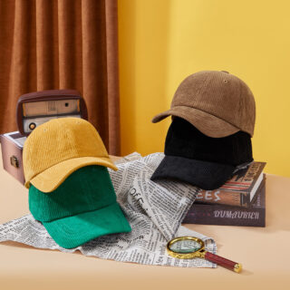 Photo de 4 casquettes en velours posé sur un bureau, deux l'une sur l'autre sur un journal et deux l'une sur l'autre sur des livres avec en arrière plan un rideau marron et un mur jaune
