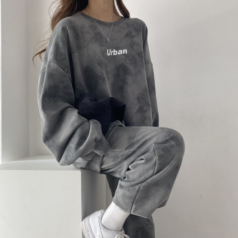 Femme portant un jogging gris et des chaussures blanches assise sur un rebord blanc