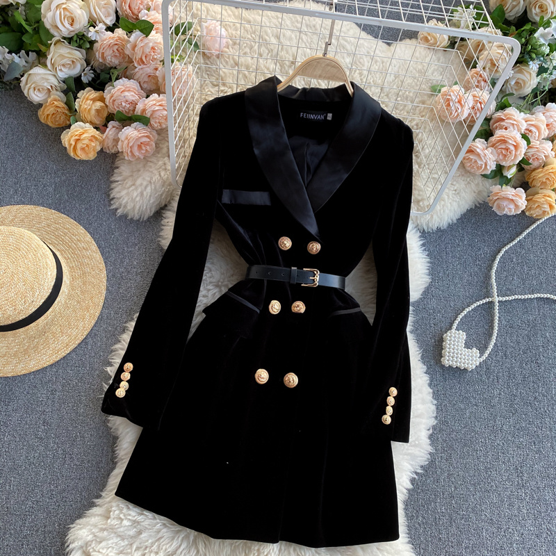 On voit un manteau noir long en velours avec un double boutonnage doré. Il est entouré de roses, d'un chapeau de paille et d'un tapis en fausse fourrure de mouton.