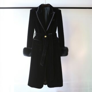 On voit un manteau long noir, en velours, suspendu à une tringle noire. Les manches sont décorées de fausses fourrures et le col en V est très élégant.