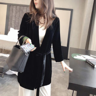 On voit une jeune femme brune qui se trouve dans une chambre d'hôtel et qui porte un mantzeau noir en velours mi-saison japonisant, coupe blazer.