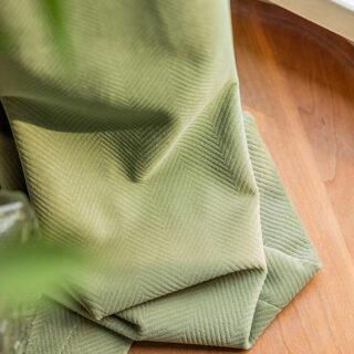 On voit un rideau en velours vert sauge qui traîne sur du parquet.