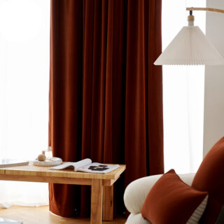 On voit un salon très bien décoré avec un rideau marron caramel en velours qui ferme une grande baie vitrée.