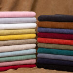 Pile de tissus côtelée de plusieurs couleur sur fond marron