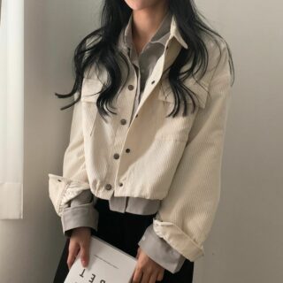 On voit une femme brune qui porte une veste en velours côtelé blanche. elle tient un livre dans ses mains.